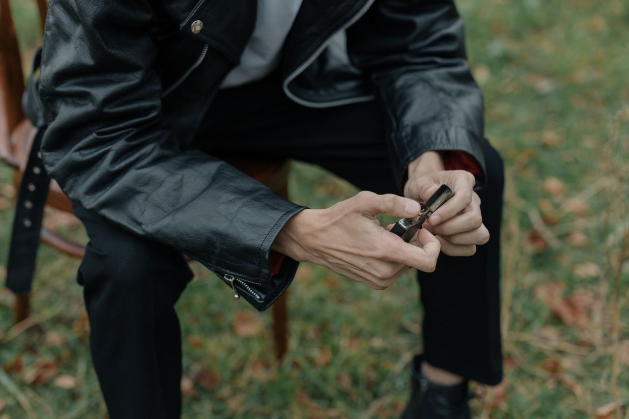 Mastering the First Impression: Your intriguing post title goes here A person in a leather jacket holding a lighter while sitting outdoors on grass.